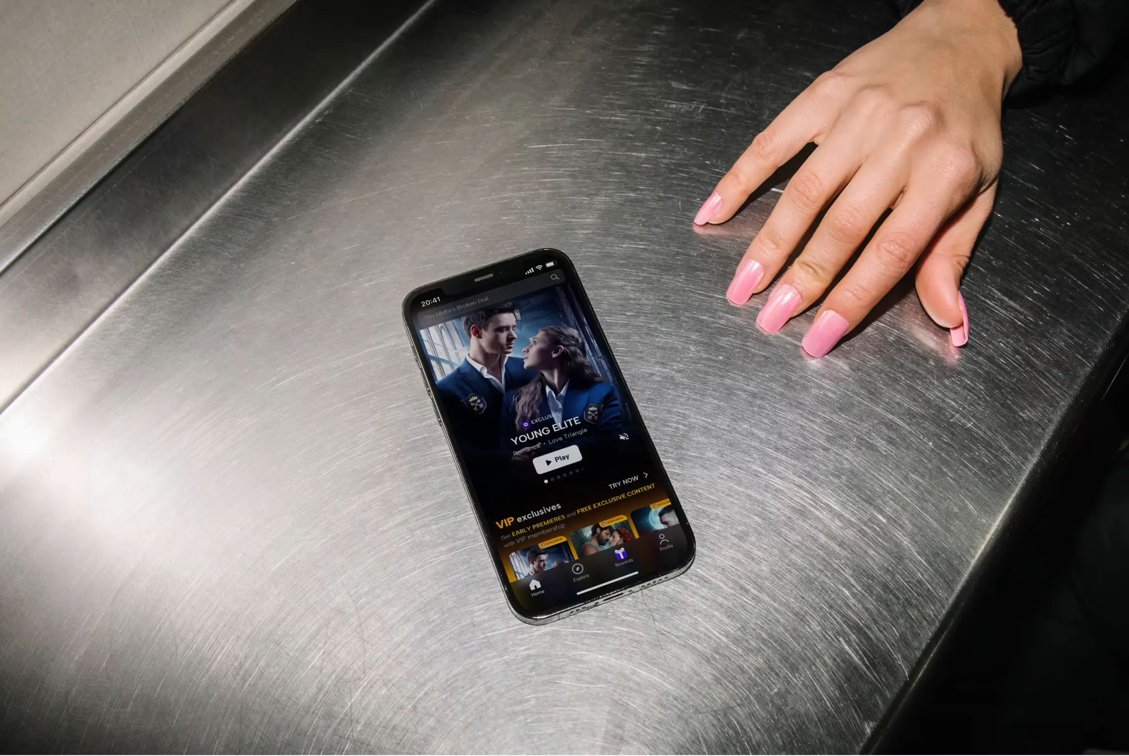 Smartphone displaying streaming content with a person's hand on a metallic surface.